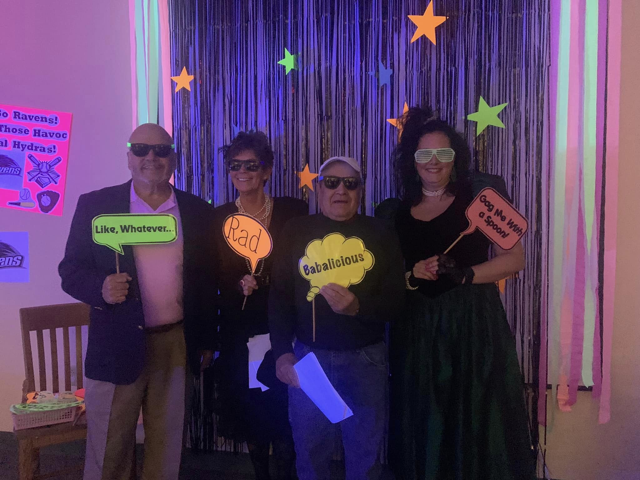 Several attendees of the library's 80s Prom Murder Mystery Fundraiser pose in front of the selfie wall showing off their totally rad outfits.